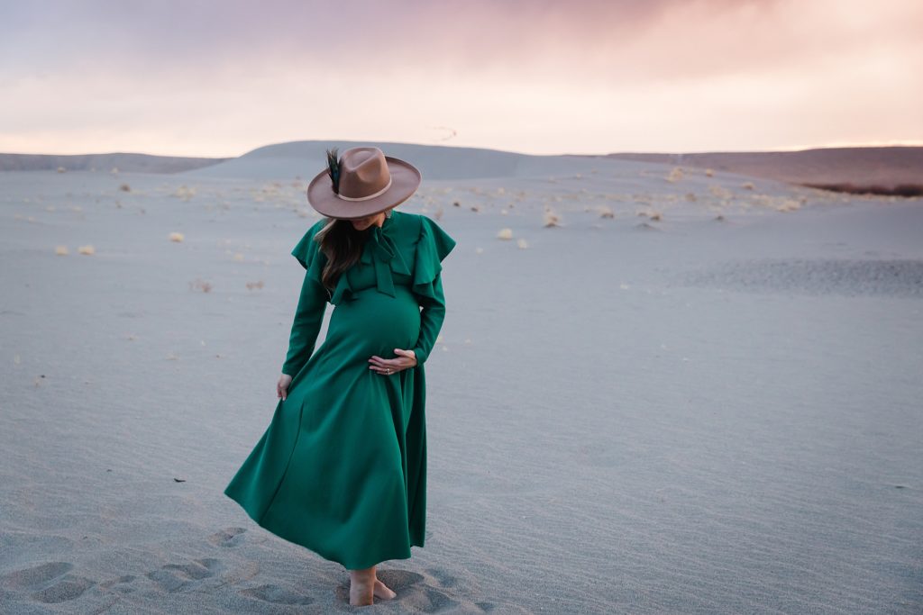 Woman in green maternity dress and felt hat walking on Bruneau Sand Dunes
