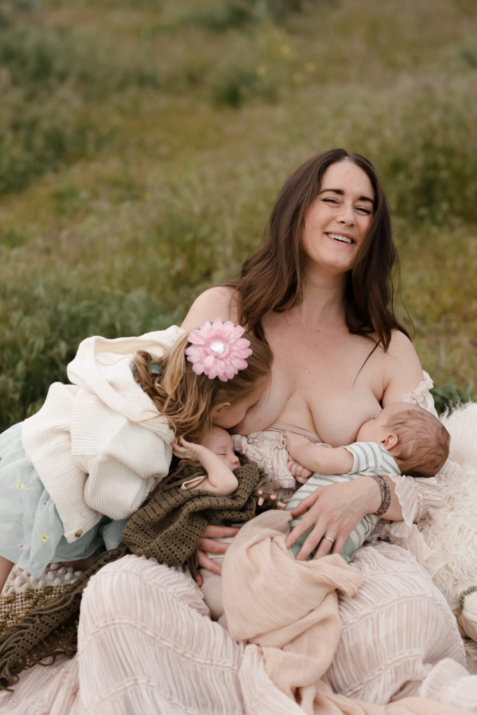 Mom laughing while she nurses her babies in a field