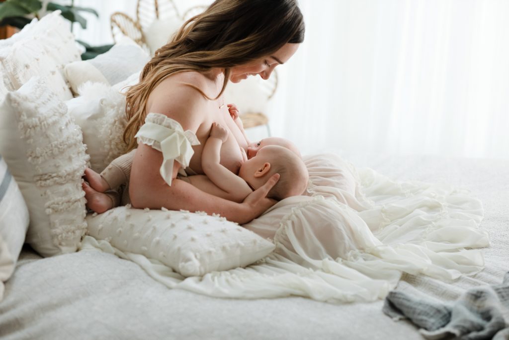 Mother breastfeeding twins on bed