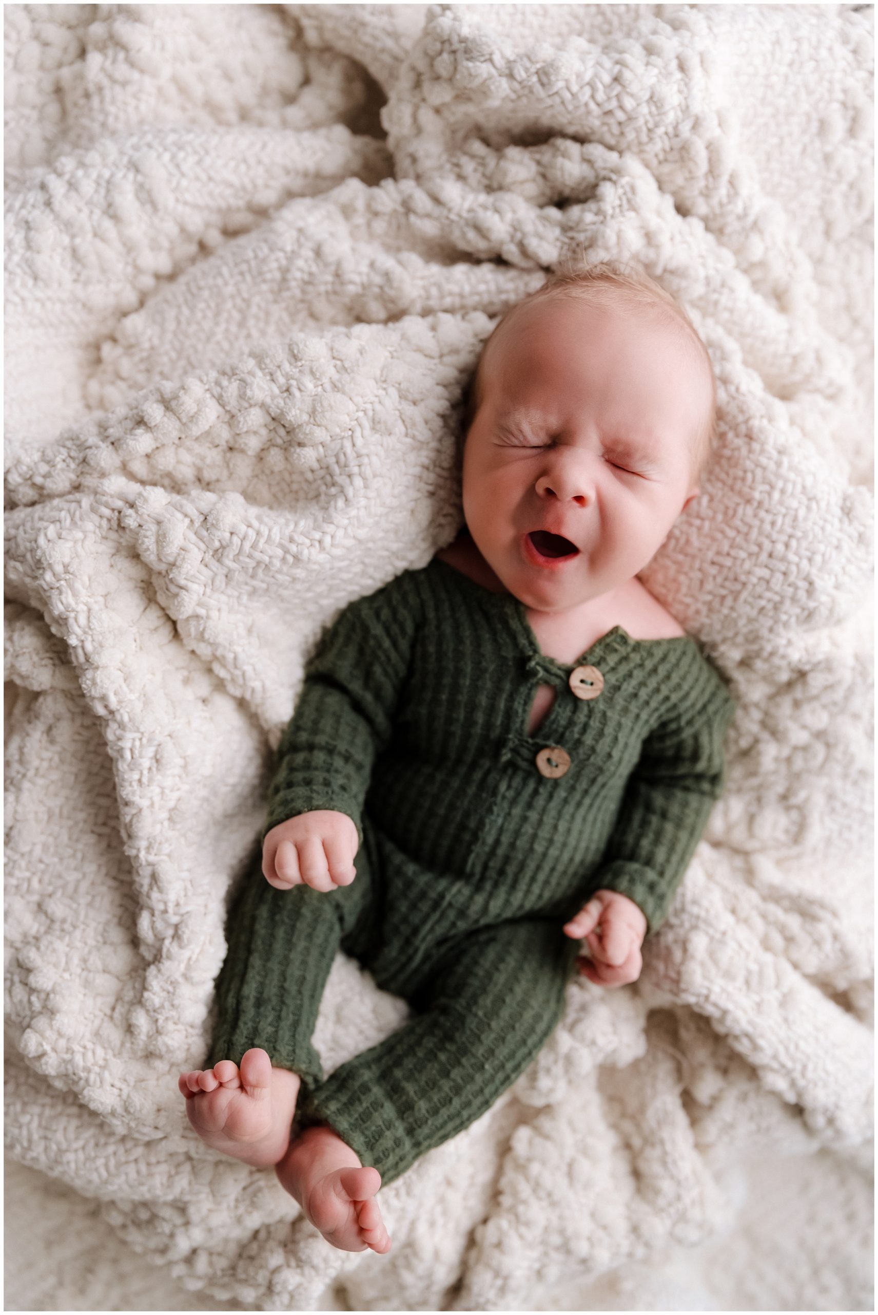 Newborn boy in green pajamas yawning