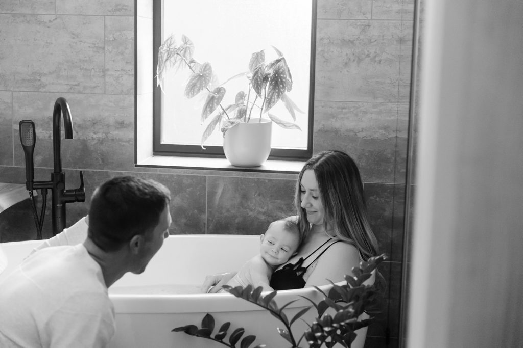 Mom holding baby in bathtub while Dad makes baby smile