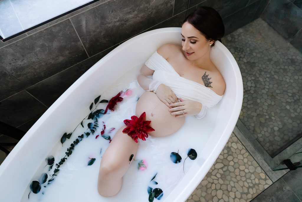 Woman in maternity milk bath with red flowers and greenery