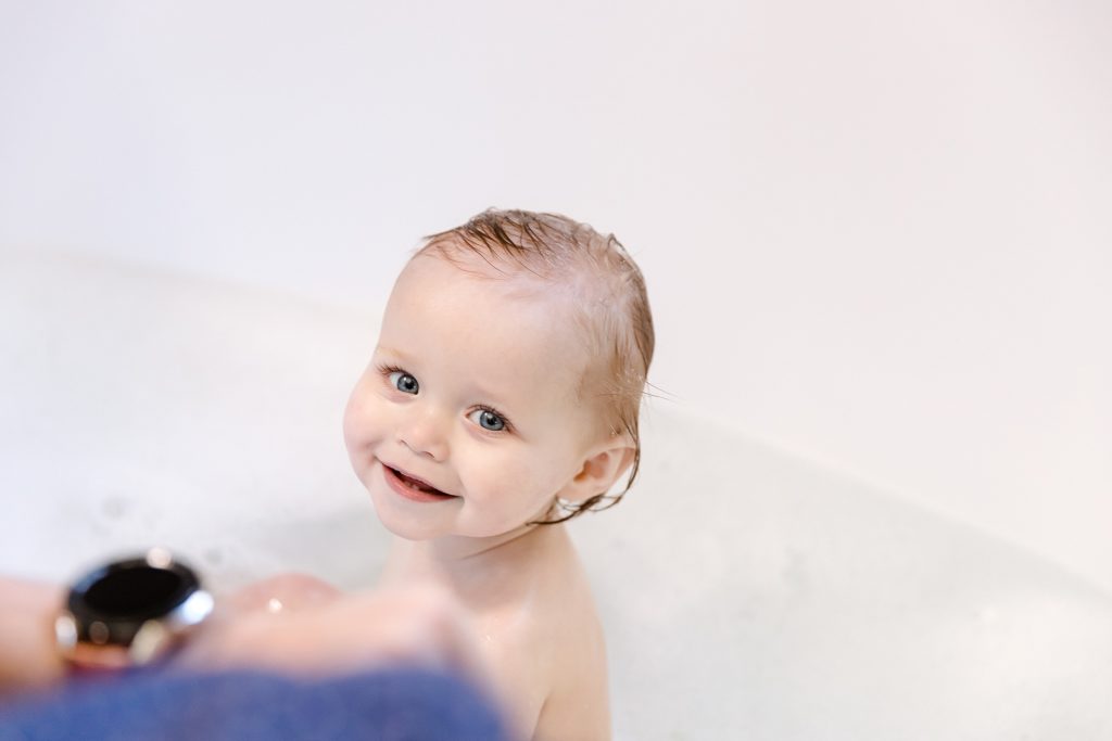 Baby with wet hair sitting in tub and smiling