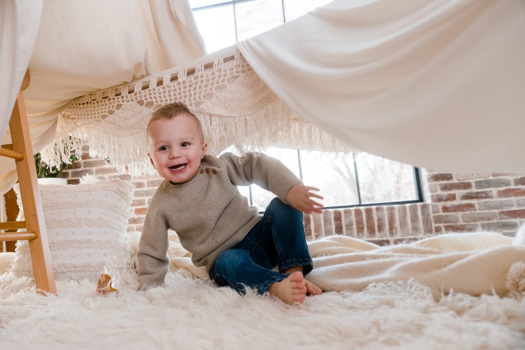 Toddler boy playing in blanket fort