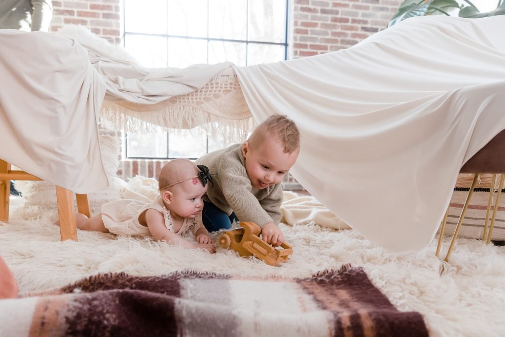 Young siblings playing with wooden toy under blanket fort
