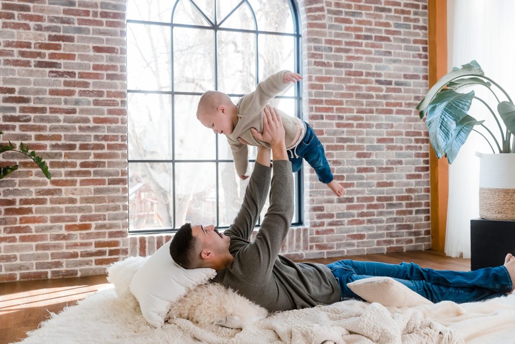 Father playing with child on rug in front of window