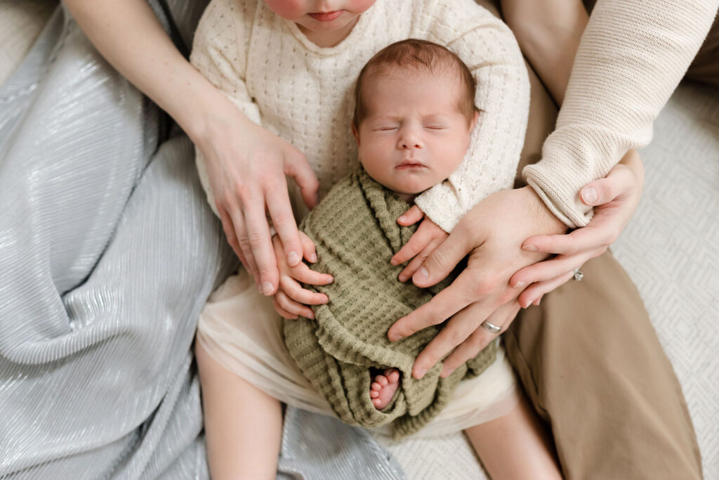 baby only photo that includes parents and sibling's hands