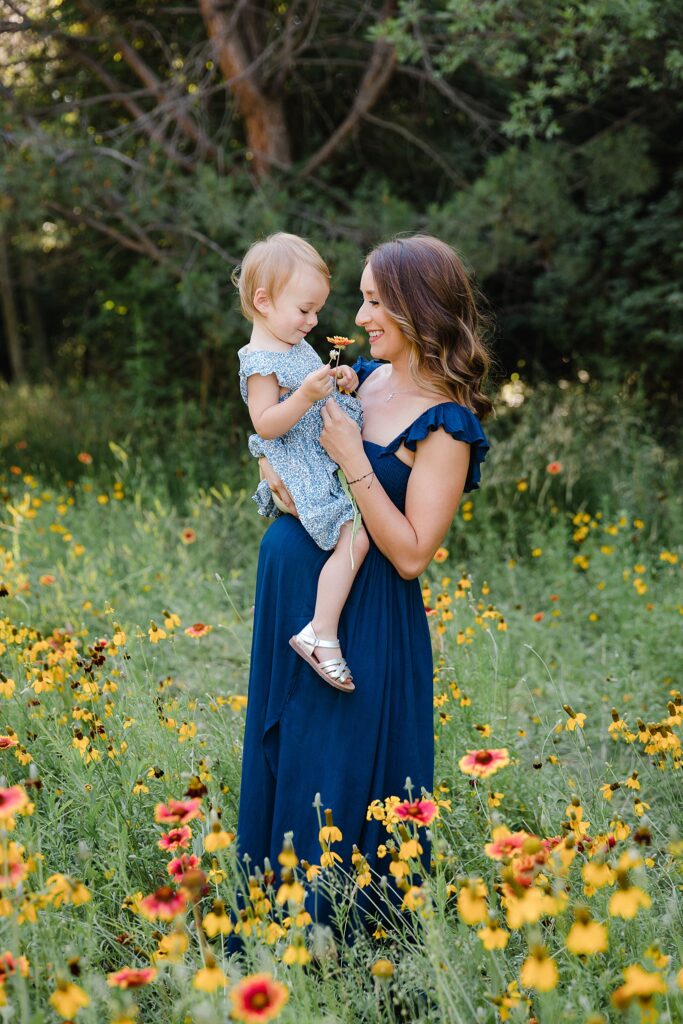 Mom in blue dress holding daughter in field of poppies and coneflowers