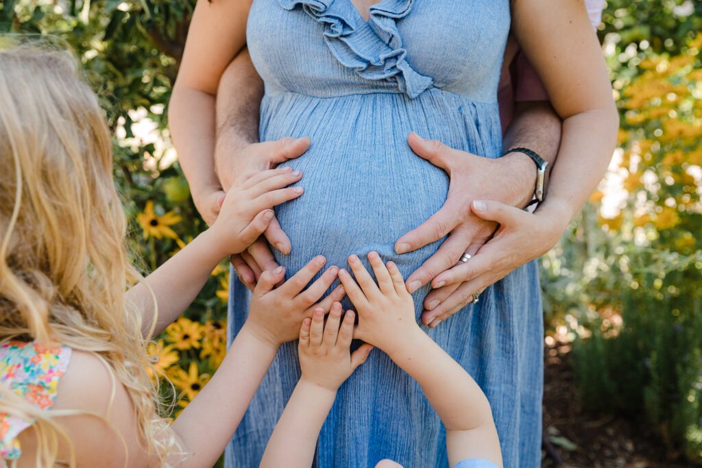 Family putting hands on mom's belly during an outdoor maternity photoshoot
