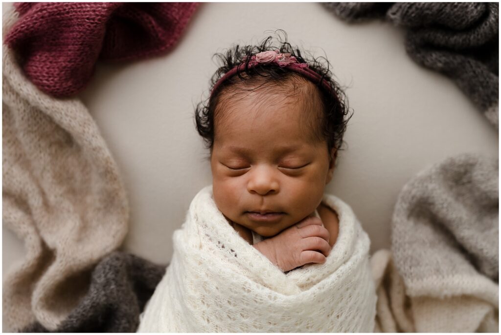 Newborn African-American baby in white swaddle with pink floral headband