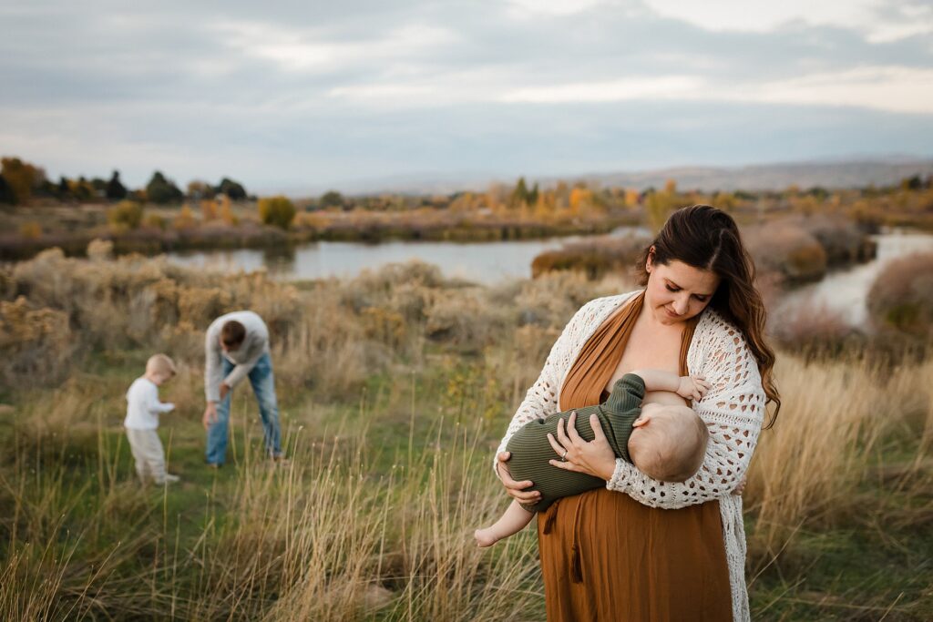 Mother nursing baby while father and older son play in background