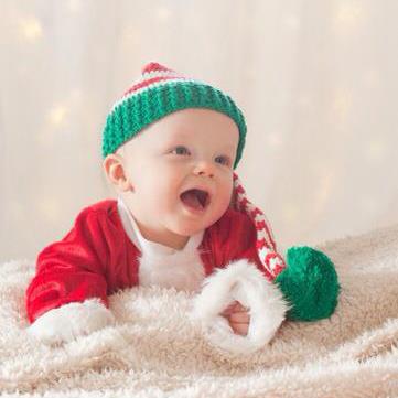 baby on fuzzy blanket wearing an elf hat and a santa coat
