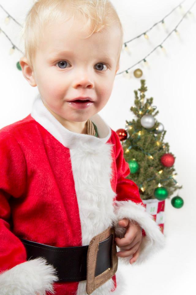 toddler in santa costume standing in front of a mini christmas tree