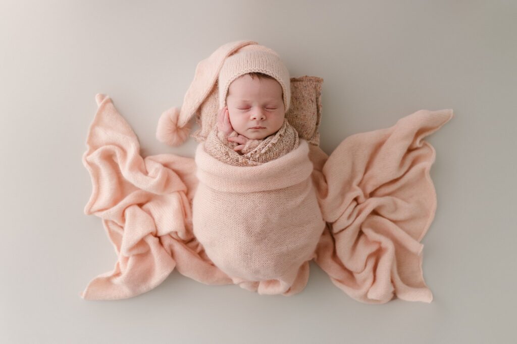 sleeping newborn baby girl in a soft pink blanket arranged around her to look like butterfly wings