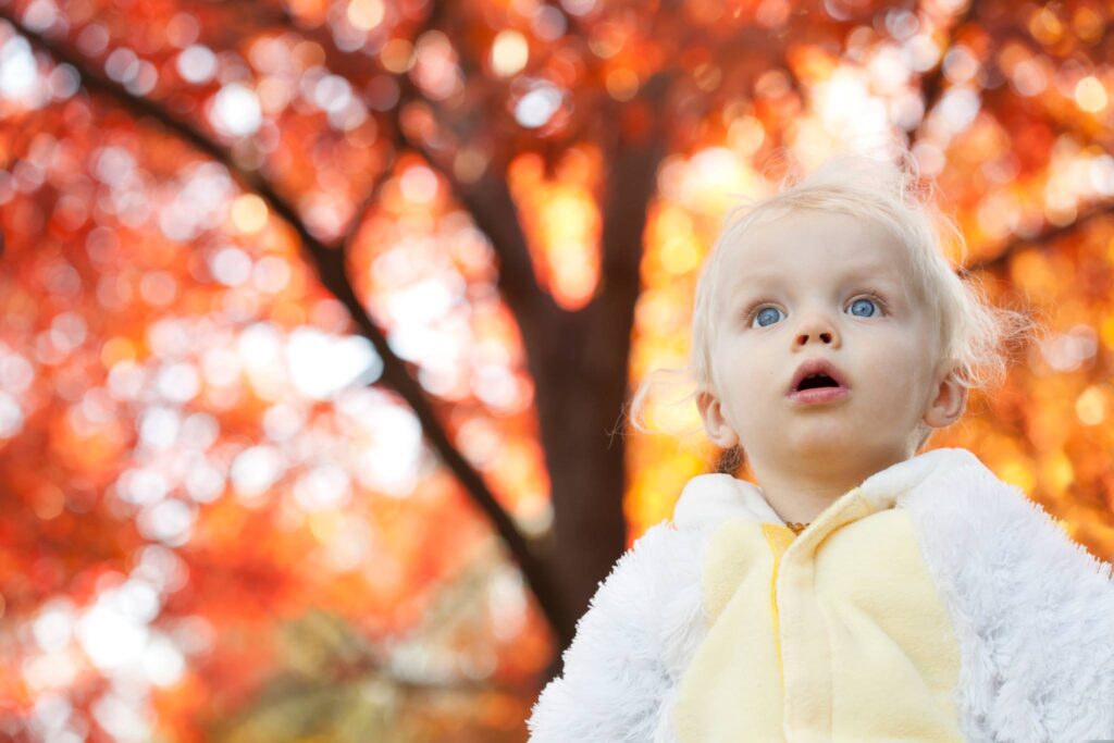 Close-up of smiling child wearing chicken costume  with orange and red fall foliage in background