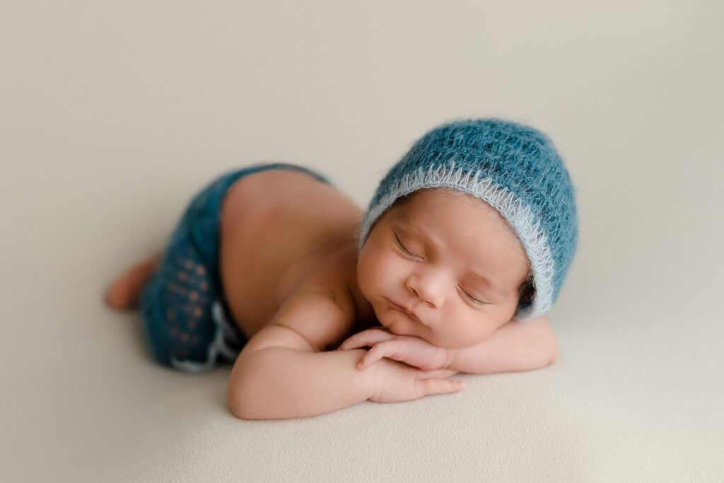 professional photo of a newborn baby boy sleeping on his tummy in a teal blue bonnet and matching knit pants