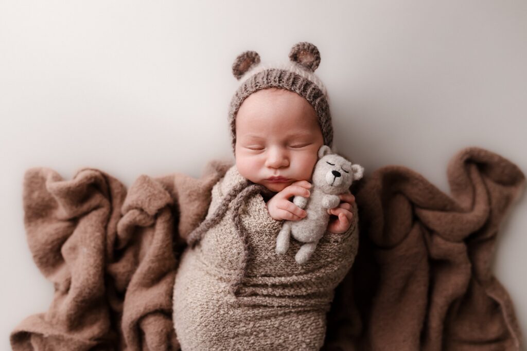 a newborn baby boy in a teddy bear hat, snuggling a felted bear the perfect gift for a new parent