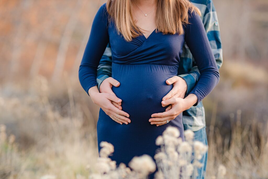 Coordinated couple's maternity photo outfits with mother in navy dress complemented by father's plaid shirt as he cradles her belly