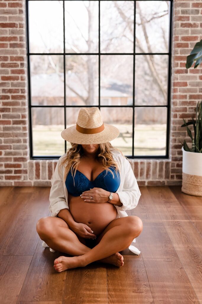 Casual summer maternity photo outfit combining white shirt, blue bralette and sun hat for a relaxed belly portrait