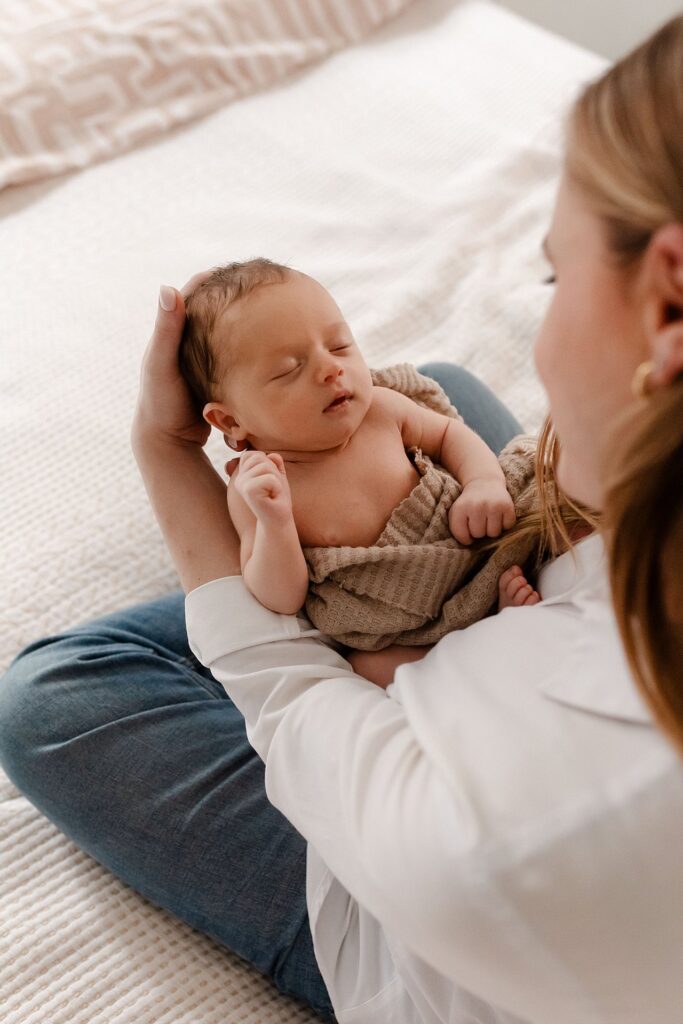 A serene portrait of maternal connection showing a mother looking down at her sleeping newborn son in her arms, capturing the quiet moments of early motherhood