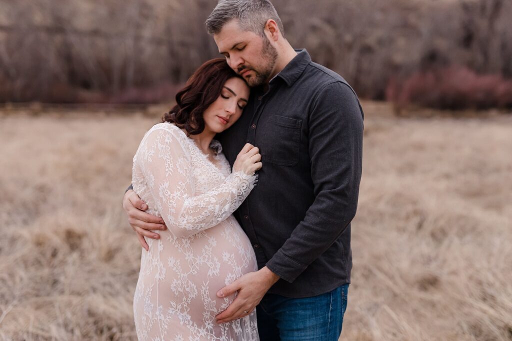 Romantic maternity portrait of couple embracing, featuring mother-to-be in an elegant fitted white dress that offers modest coverage