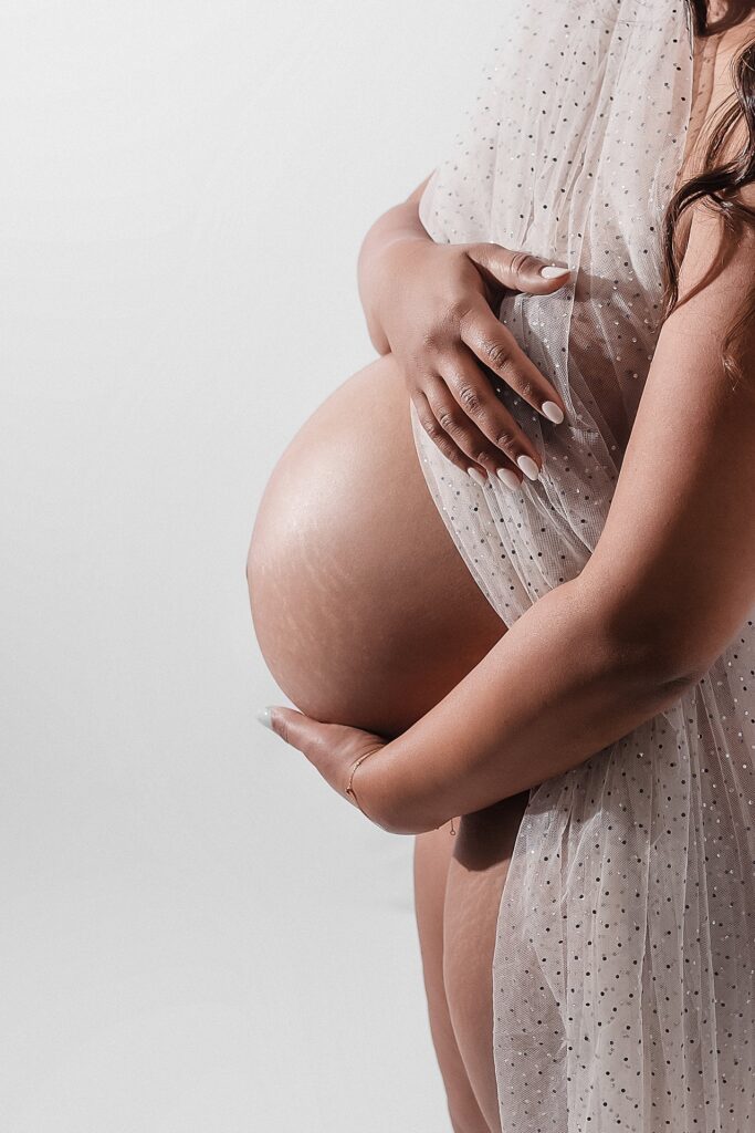 Artistic maternity photo with sheer fabric draped over pregnant belly creating ethereal light and shadow