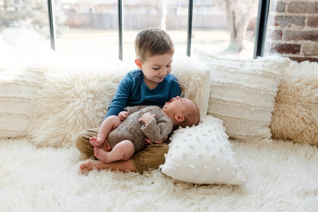 a big brother holding his new little brother during his newborn photoshoot.