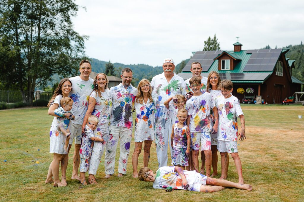 Extended family standing together in a field, joyfully covered in colorful paint after what was clearly an unforgettable day together. This image perfectly demonstrates the importance of printed photographs in preserving not just posed moments, but the messy, authentic experiences that bring families together—memories that might fade from our minds but remain vibrant and accessible when captured in print and displayed in our homes.