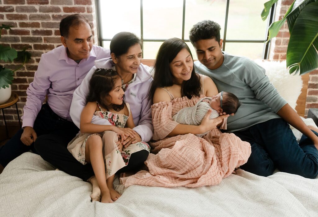 Three generations gathered in one frame: grandparents beaming with pride alongside mom, dad, big sister, and newborn baby. This wall-worthy family portrait demonstrates the importance of printed photographs.