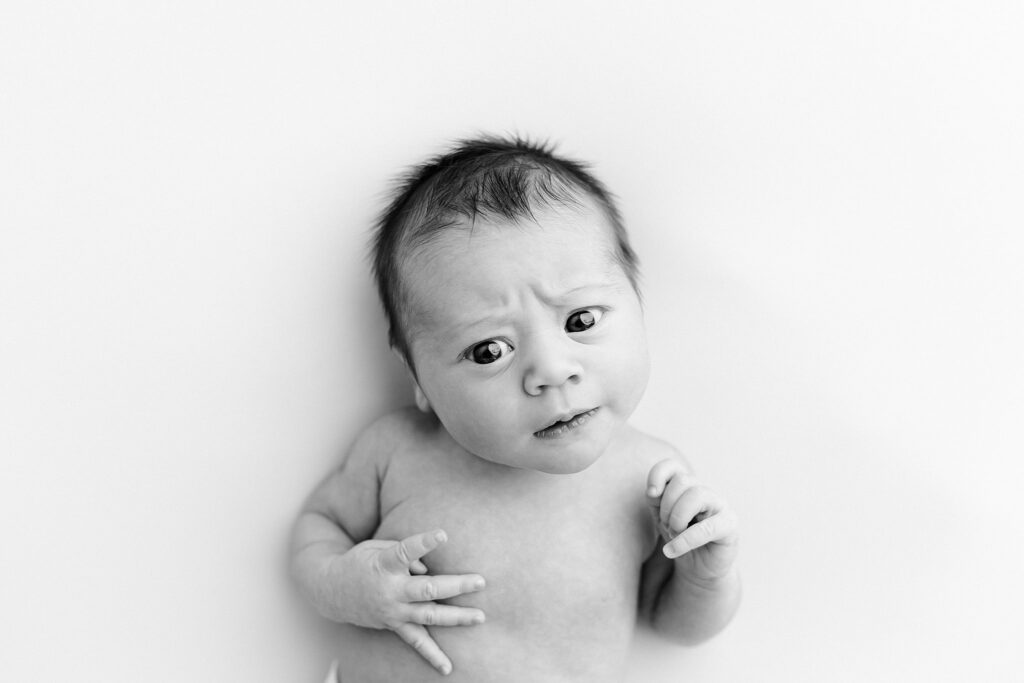 a newborn baby in a black and white photo looking skeptical toward the camera.