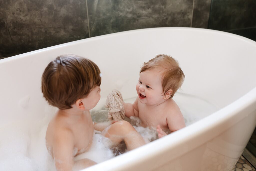 Post-cake smash cleanup in the studio's soaker tub - little girl washes away pink frosting, pure joy captured during the splash bath finale