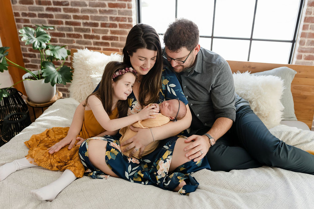 Family surrounding a new baby girl in a yellow wrap during a newborn session with glean and co