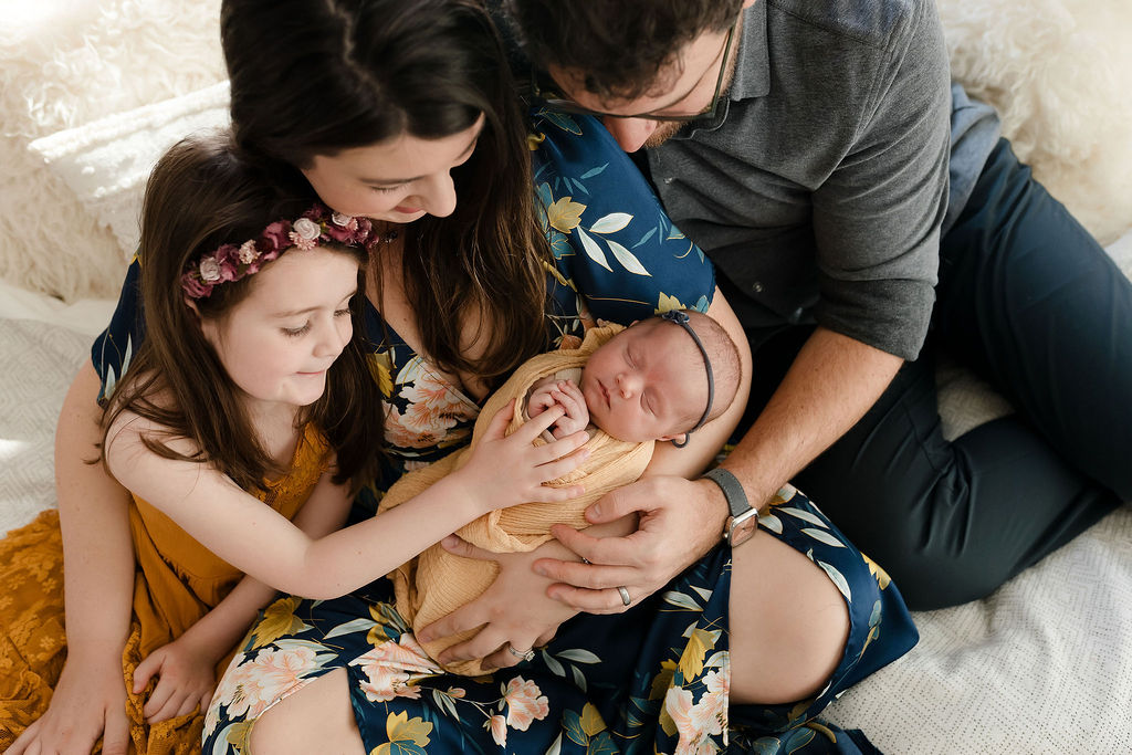 mom, dad, big sister, and baby sister snuggled together during a mini newborn session