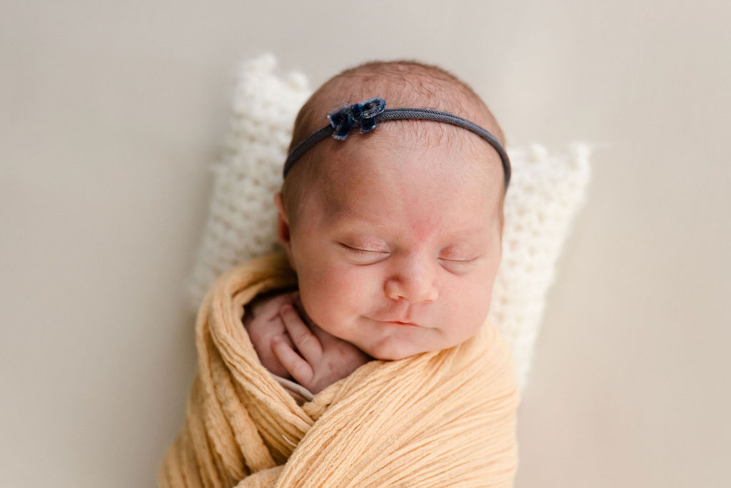 newborn baby girl in a yellow wrap with a tiny blue headband