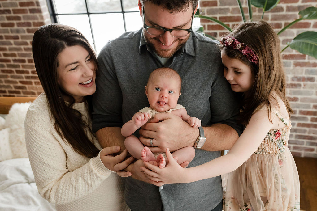 a silly family portrait of a newborn baby sticking out her tongue surrounded by her mom, dad and big sister