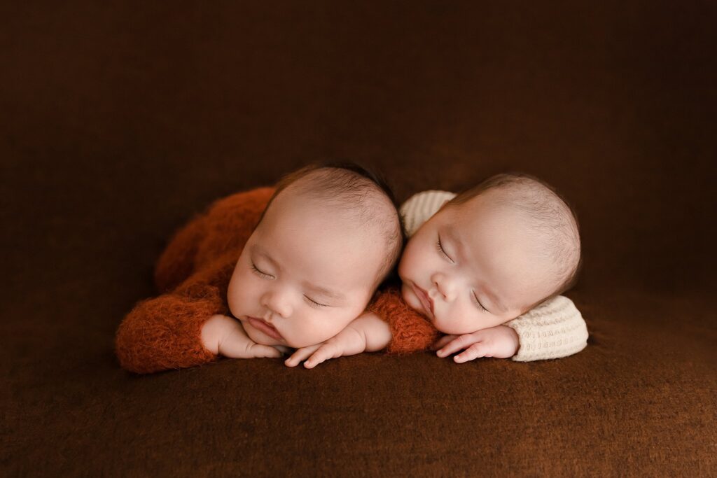 Newborn twin babies cuddling together on a rust colored blanket to match their fall maternity photo shoot