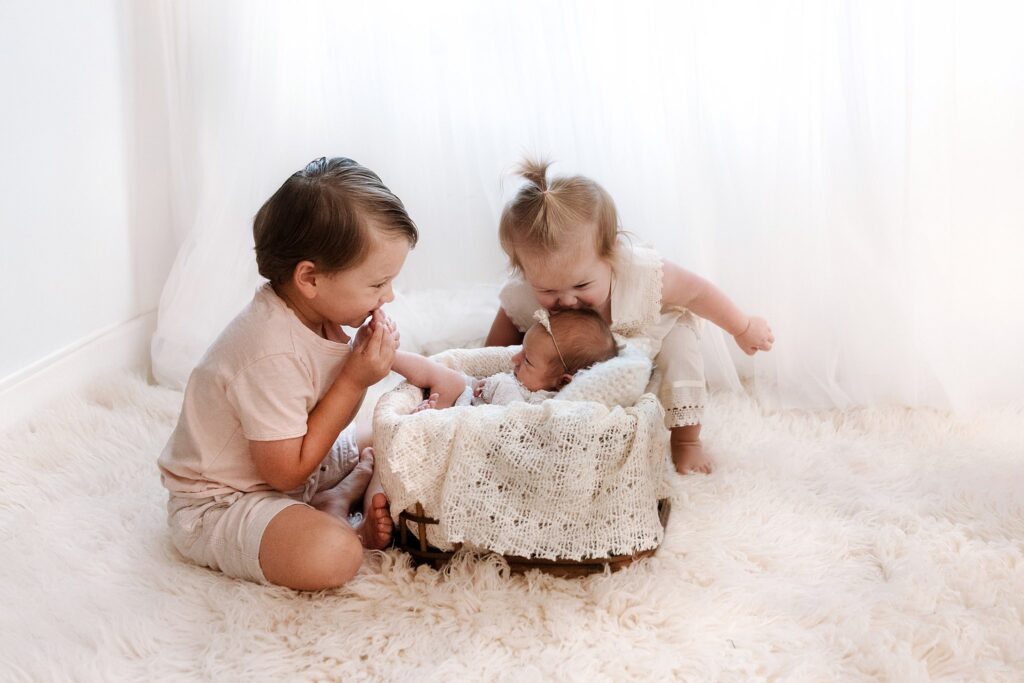 Young boy and toddler girl posing with newborn baby in wicker basket showing how to prepare child for new baby through photography