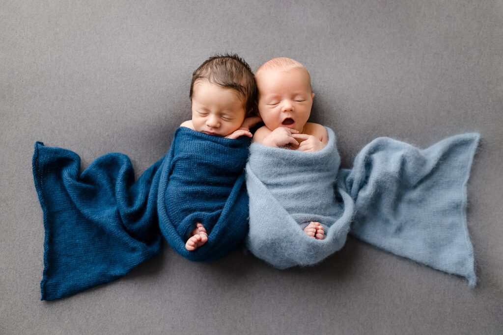 twin newborn baby boys wrapped in a dark blue wrap and a light blue warp contrasting them for their newborn twin photography session