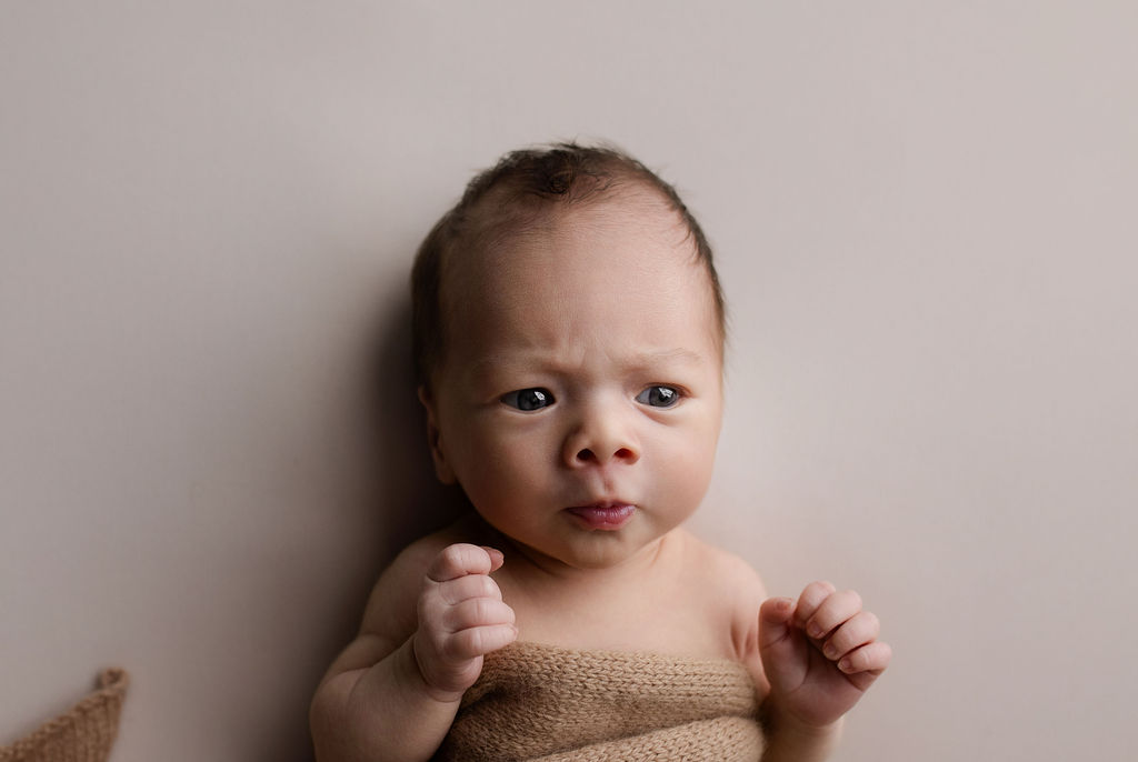 Alert newborn baby wrapped in tan knit blanket during relaxed newborn photography session