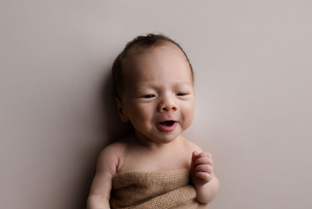 Smiling newborn baby in tan wrap showing natural personality expressions