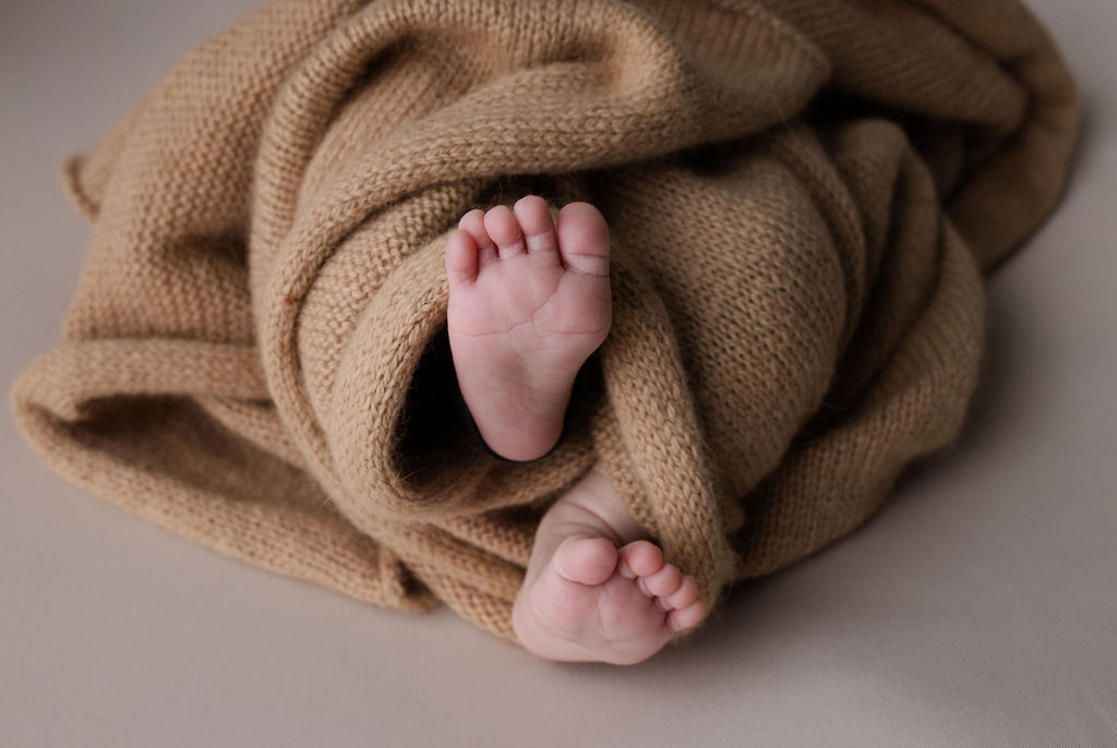 Newborn baby feet peeking through soft tan knit blanket during a relaxed newborn photoshoot with Glean and Co Photography in Boise Idaho