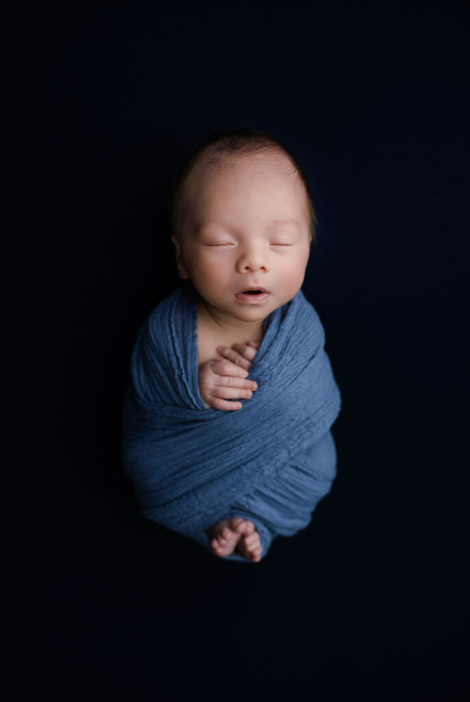Peacefully sleeping newborn wrapped in blue against dark background