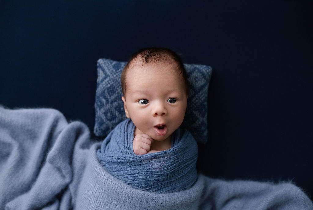 Wide-eyed alert newborn baby in blue wrap showing natural expressions