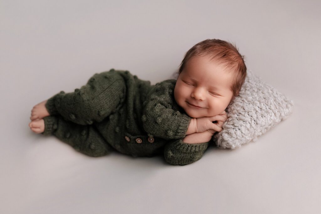 sleeping newborn baby boy smiling while lying on his side during professional session with best newborn photographer Boise