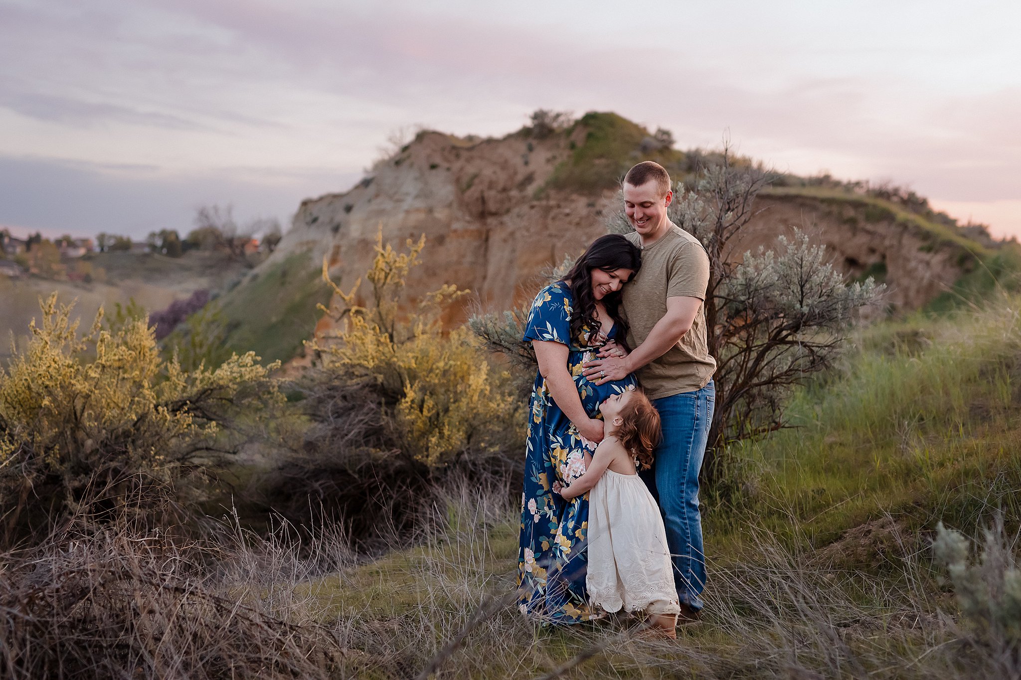 Pregnant mother and toddler daughter embracing in front of sandstone cliffs during Boise location scouting for family photos maternity session at Foothills Learning Center