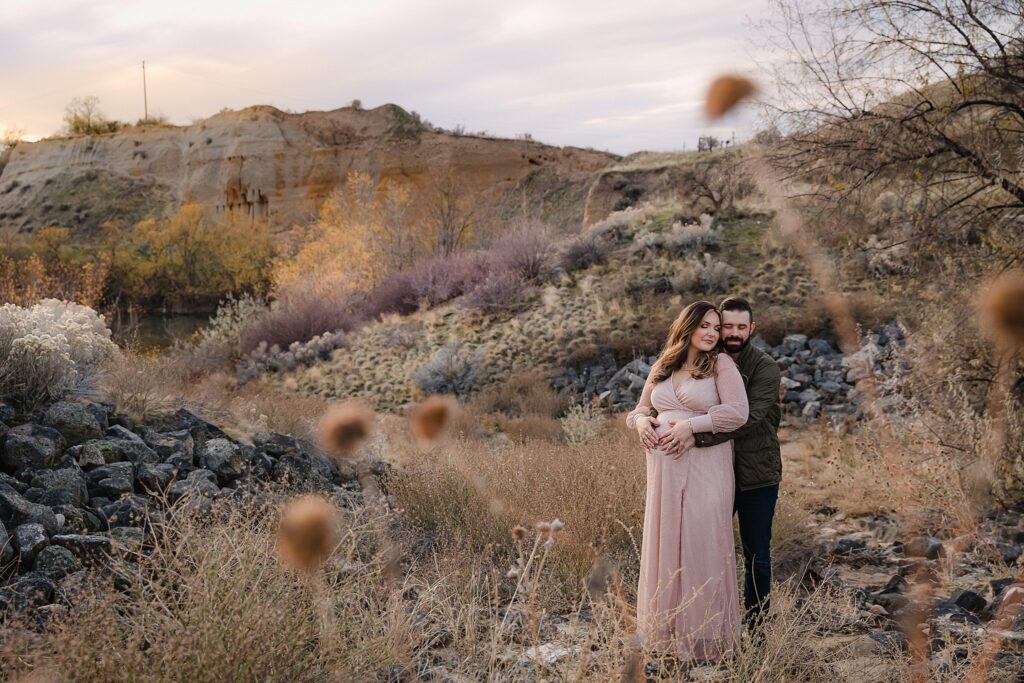 Boise maternity portrait against warm sandstone cliffs with golden dormant grasses, bare sage and purple during late fall session