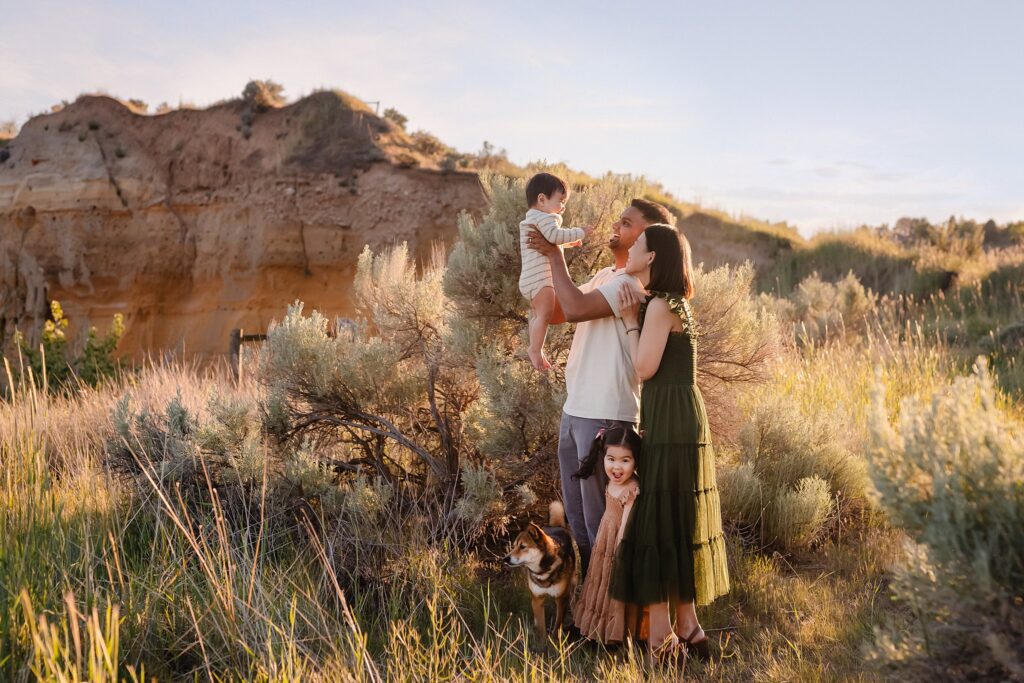 Family of four posing in front of sandstone rock formation surrounded by green sage brush and warm summer sun at Foothills Learning Center