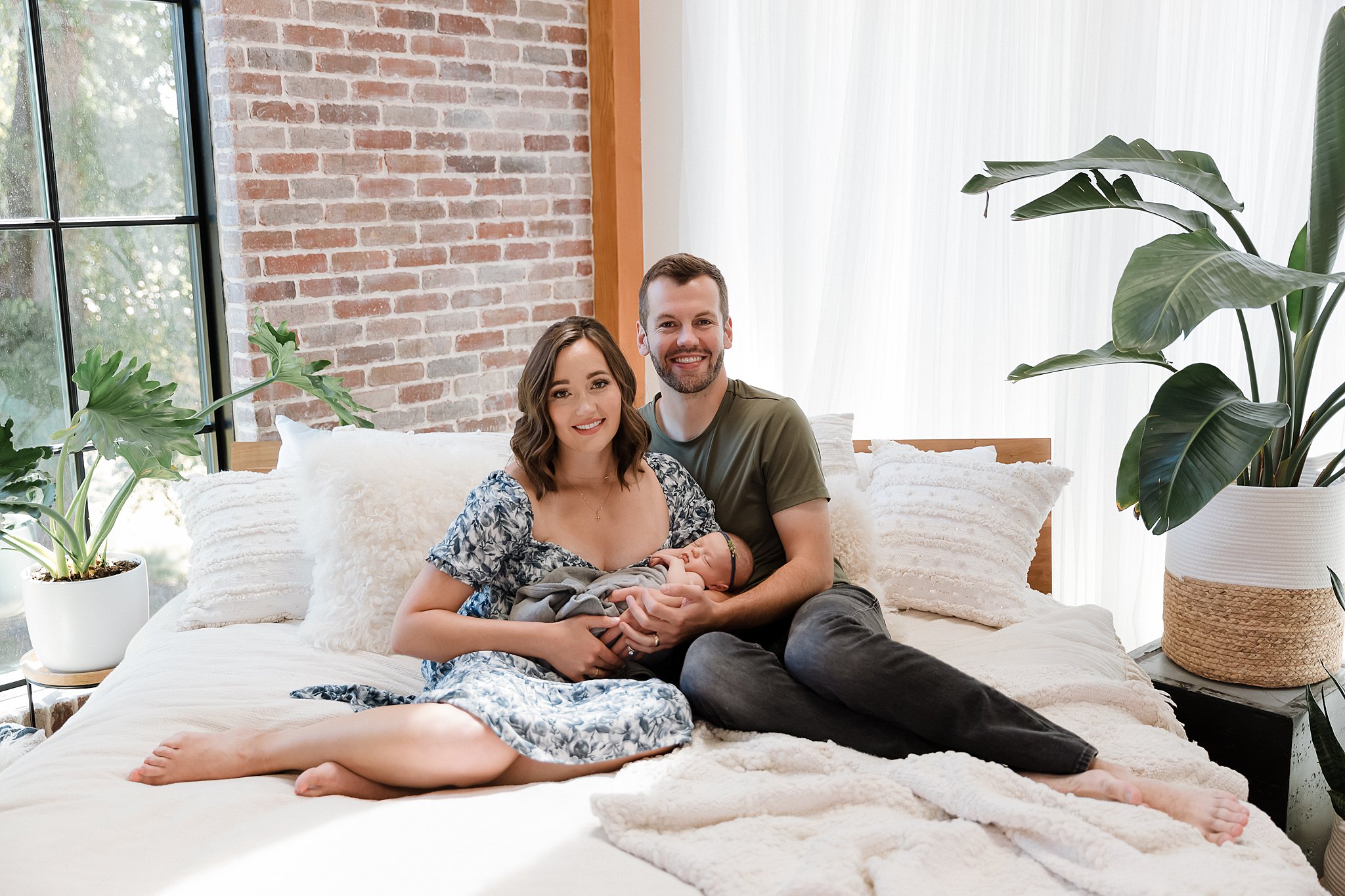 Relaxed lifestyle newborn portrait of parents snuggling their baby in comfortable, home-like studio environment with natural window light