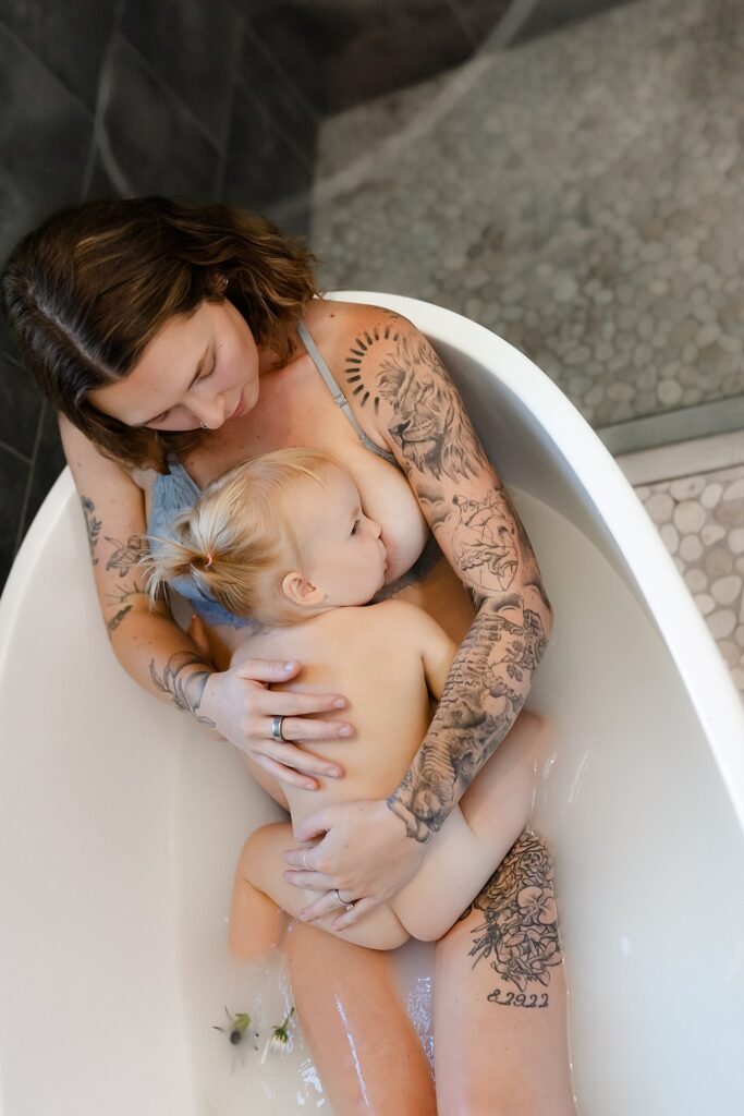 Professional breastfeeding photography showcasing tattooed pregnant mom and daughter connection in breast milk bath with botanical elements at luxury Boise studio