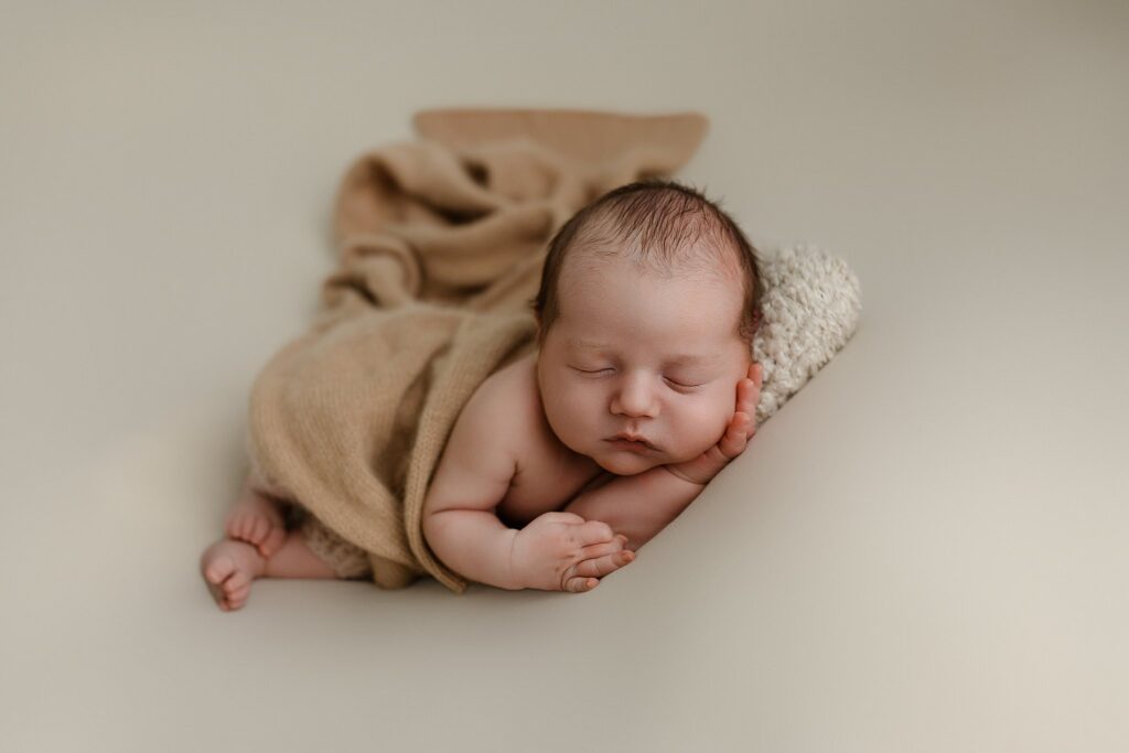 Sleeping newborn baby posed in tan wrap on cream backdrop at Glean and Co Photography studio in Boise Idaho